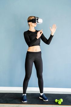 Fitness, sport and technology. Young athletic woman wearing virtual reality glasses standing at fitness mat using VR interactive menu