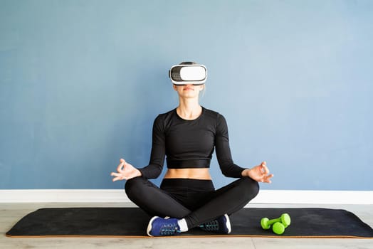 Fitness, sport and technology. Young athletic woman wearing virtual reality glasses doing yoga on fitness mat