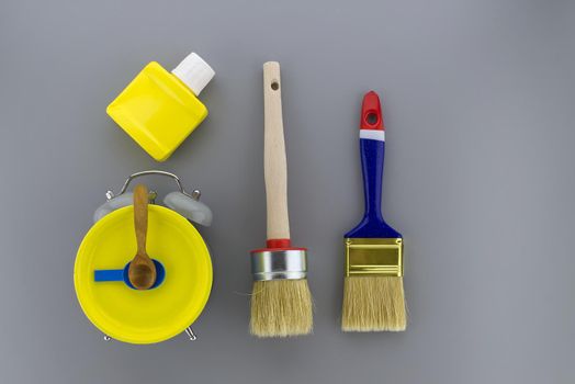 Creative DIY, decorating or renovations background with two clean bristle brushes and a colorful yellow alarm clock with tools for hands forming a border on grey with copy space