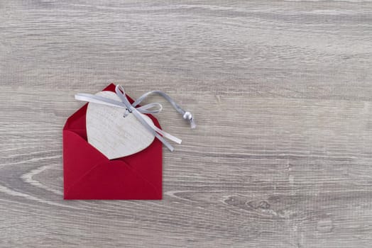 A heart-shaped wooden medallion is placed in a red envelope. Greetings and love letter