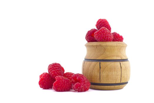 Pile of red ripe raspberry berries and a small wooden pot isolated on white background