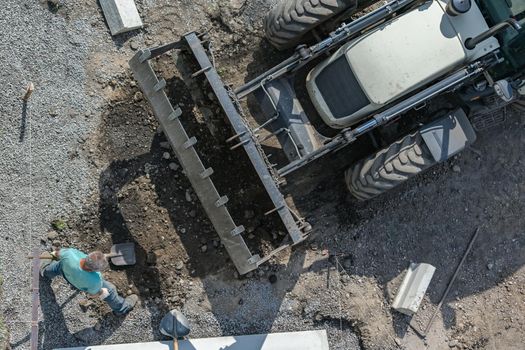 A worker loads soil into an excavator bucket with a shovel during road construction