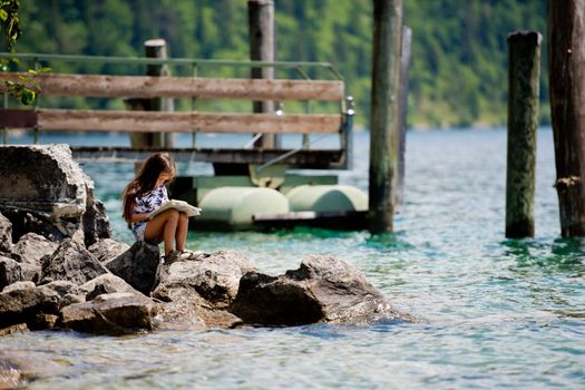 A little sweet girl sits on the shore of the Alpine lake Plansee and looks at the map. Plansee lake, Austria.