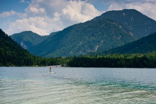 A young man is standing on a board with a paddle on the lake.