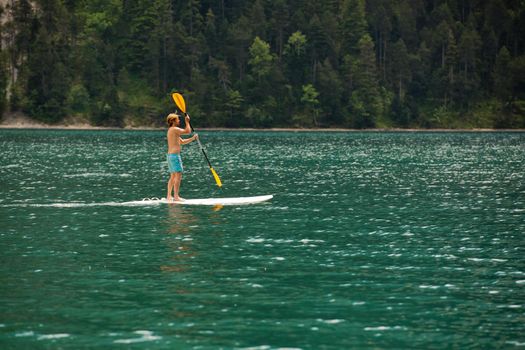 A young man is standing on a board with a paddle on the lake.