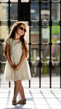 A little sweet girl in a white dress and wearing sunglasses.