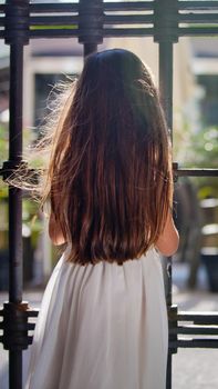 A little sweet girl in a white dress and long dark hair. View from the back.