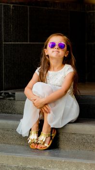 Portrait of a little girl in a white dress in sunglasses.