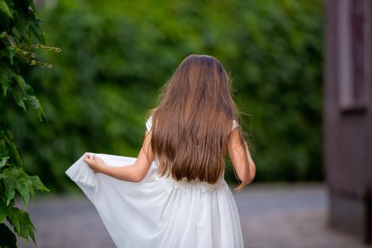 Cute girl in white dress is standing with her back on a green fence background. Close-up.