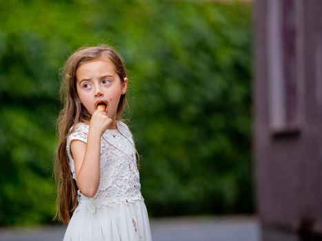 A little girl in a white dress is eating ice cream.