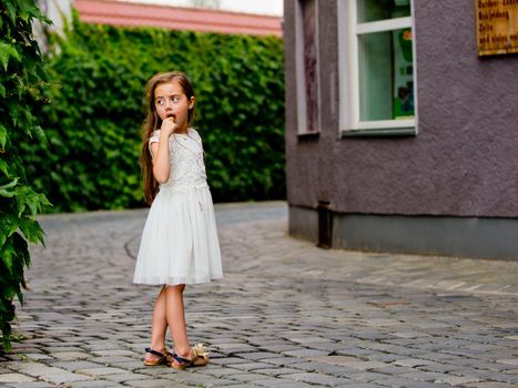 A little girl in a white dress is eating ice cream.