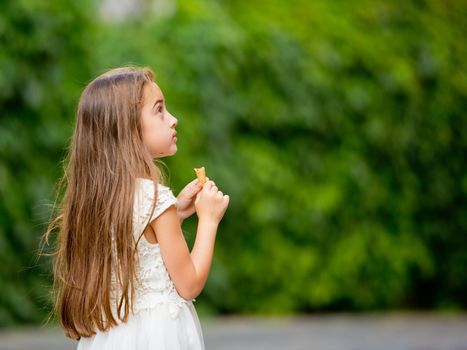 A little girl in a white dress is eating ice cream.