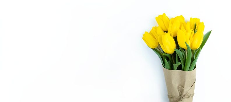 Bouquet of yellow tulips wrapped in craft paper on a white background with copy space.