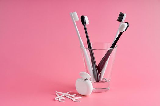 Fashionable toothbrush with soft bristles. Popular toothbrushes. Hygiene trends. Oral hygiene kit. Toothbrushes in glass, floss thread and toothpicks on a pink background.