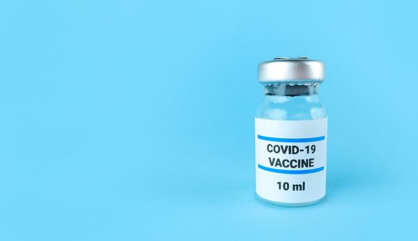 Medicine bottle with covid 19 vaccine on a blue background with copy space.