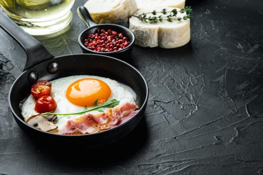 Fried eggs with cherry tomatoes and bread for breakfast in cast iron frying pan, on black background , with space for text copyspace