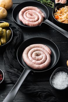 Raw meat sausage set in cast iron frying pan, on black wooden table background