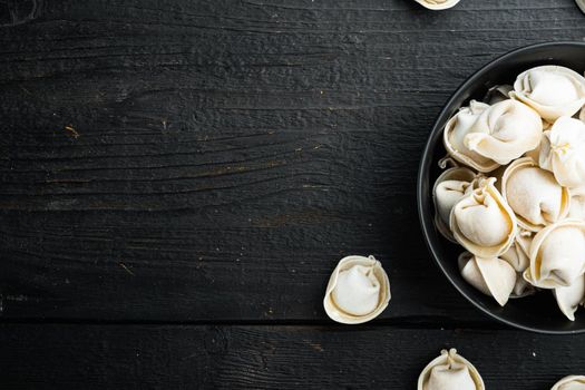 Frozen dumplings tortellini and ravioli set in black bowl, on black wooden table background, top view flat lay , with copyspace and space for text