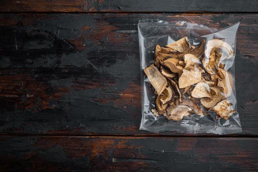 Dried wild mushrooms set, on old dark wooden table background, in plastic pack, top view flat lay , with space for text copyspace