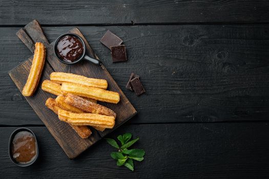 Traditional Spanish dessert churros with sugar and chocolate set, on black wooden table background, top view flat lay with space for text, copyspace