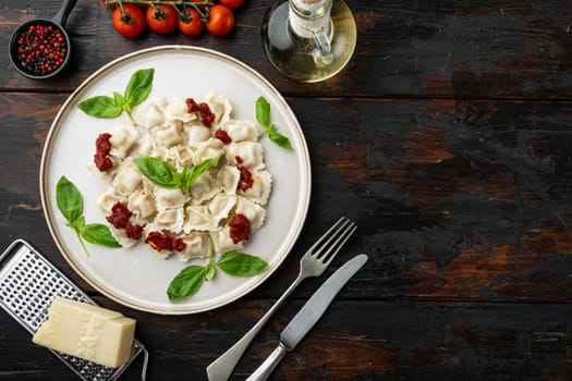 Appetizing ravioli with tomato sauce, cheese and basil set with basil parmesan and tomatoe on white plate on old dark wooden table background, top view flat lay , with copyspace and space for text