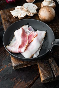 Raw bacon set in cast iron frying pan, on old dark wooden table background