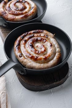Fried Bavarian pork meat spiral sausages set in cast iron frying pan, on white background