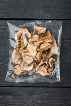 Mix of chopped wild dried mushrooms set, on black wooden table background, in plastic pack, top view flat lay