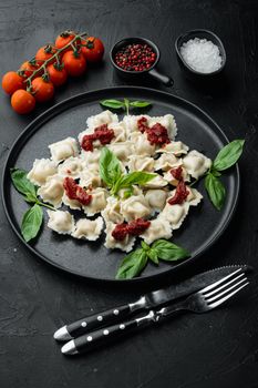 Ravioli pasta with mushroom cream sauce and cheese - Italian food style set with basil parmesan and tomatoe on black plate, on black background