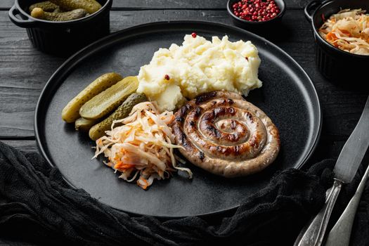 Wurst or Bratwurst with Fermented Cabbage, Pickled Cucumber, and Spices, on black wooden table background