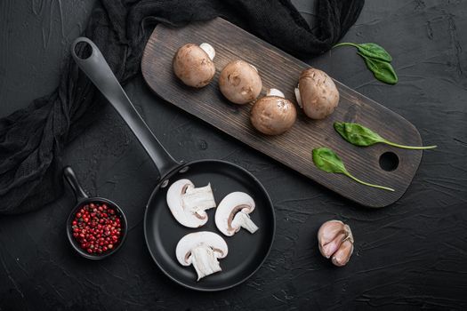 Brown champignons mushroom set in cast iron frying pan, on black background, top view flat lay
