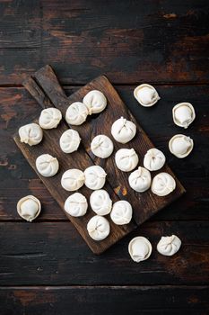Frozen dumplings tortellini and ravioli set on cutting board on old dark wooden table background, top view flat lay