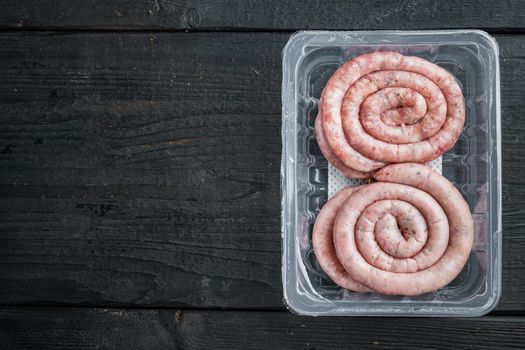 Raw meat sausage set, on black wooden table background, in plastic pack, top view flat lay , with space for text copyspace