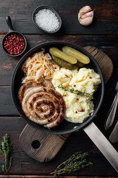 Rustic food with roasted sausage mashed potatoes and sour cabbages in cast iron frying pan, on old dark wooden table background, top view flat lay