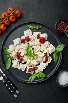 Appetizing ravioli with tomato sauce, cheese and basil set with basil parmesan and tomatoe on black plate, on black background, top view flat lay