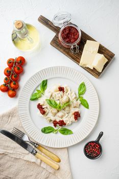 Ravioli pasta with mushroom cream sauce and cheese - Italian food style set with basil parmesan and tomatoe on white plate, on white background, top view flat lay