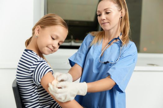 a woman doctor in a dressing gown seals a child's hand with a plaster. High quality photo