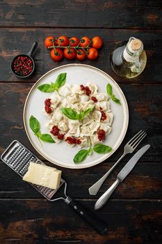 Ravioli pasta with mushroom cream sauce and cheese - Italian food style set with basil parmesan and tomatoe on white plate on old dark wooden table background, top view flat lay