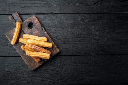 Churros sprinkled with powdered sugar set, on black wooden table background, top view flat lay with space for text, copyspace