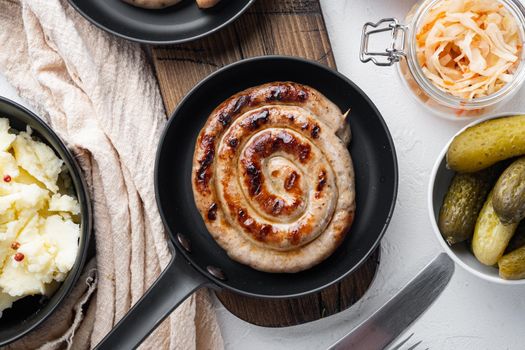 Bavarian fried sausage on sauerkraut in cast iron frying pan, on white background, top view flat lay