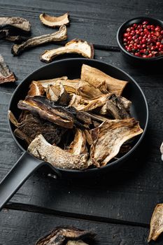 Mix of chopped wild dried mushrooms set in cast iron frying pan, on black wooden table background