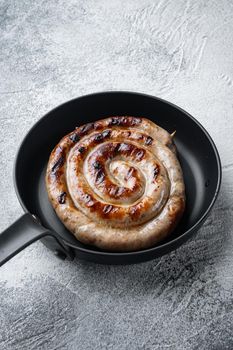 Homemade Spiral grilled sausage set in cast iron frying pan, on gray background