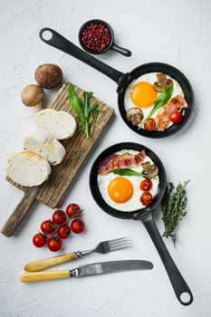 Fried eggs with cherry tomatoes and bread for breakfast in cast iron frying pan, on white background, top view flat lay