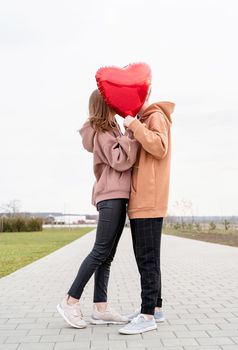 Valentines Day. Young loving couple hugging and holding red heart shaped balloon outdoors