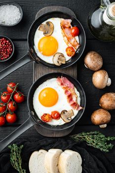 Scrambled eggs in frying pan with pork lard, bread and green feather in cast iron frying pan, on black wooden table background, top view flat lay