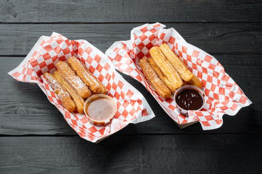 Spanish porras. Spanish food like spanish churros with chocolate, and caramel in paper tray, on black wooden table background