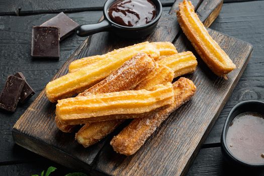 Churros with sugar, and chocolate sauce, on black wooden table background