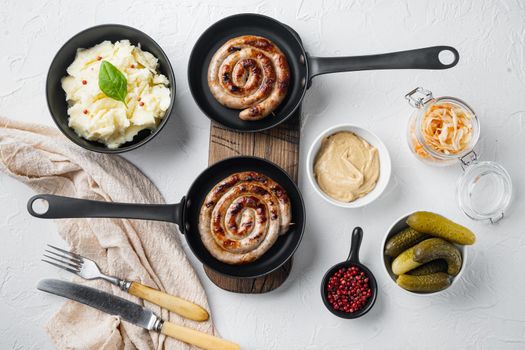 Fried Bavarian German Nurnberger sausages with sauerkraut, mashed potatoe in cast iron frying pan, on white background, top view flat lay