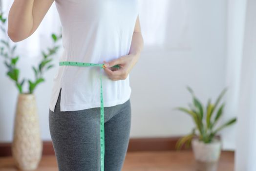 Sporty woman keep exercising with healthy nutrition measuring her slim body and thin waist with a tape measure. 