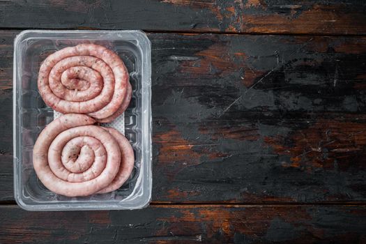 Traditional raw spiral pork sausages set, on old dark wooden table background, in plastic pack, top view flat lay , with space for text copyspace